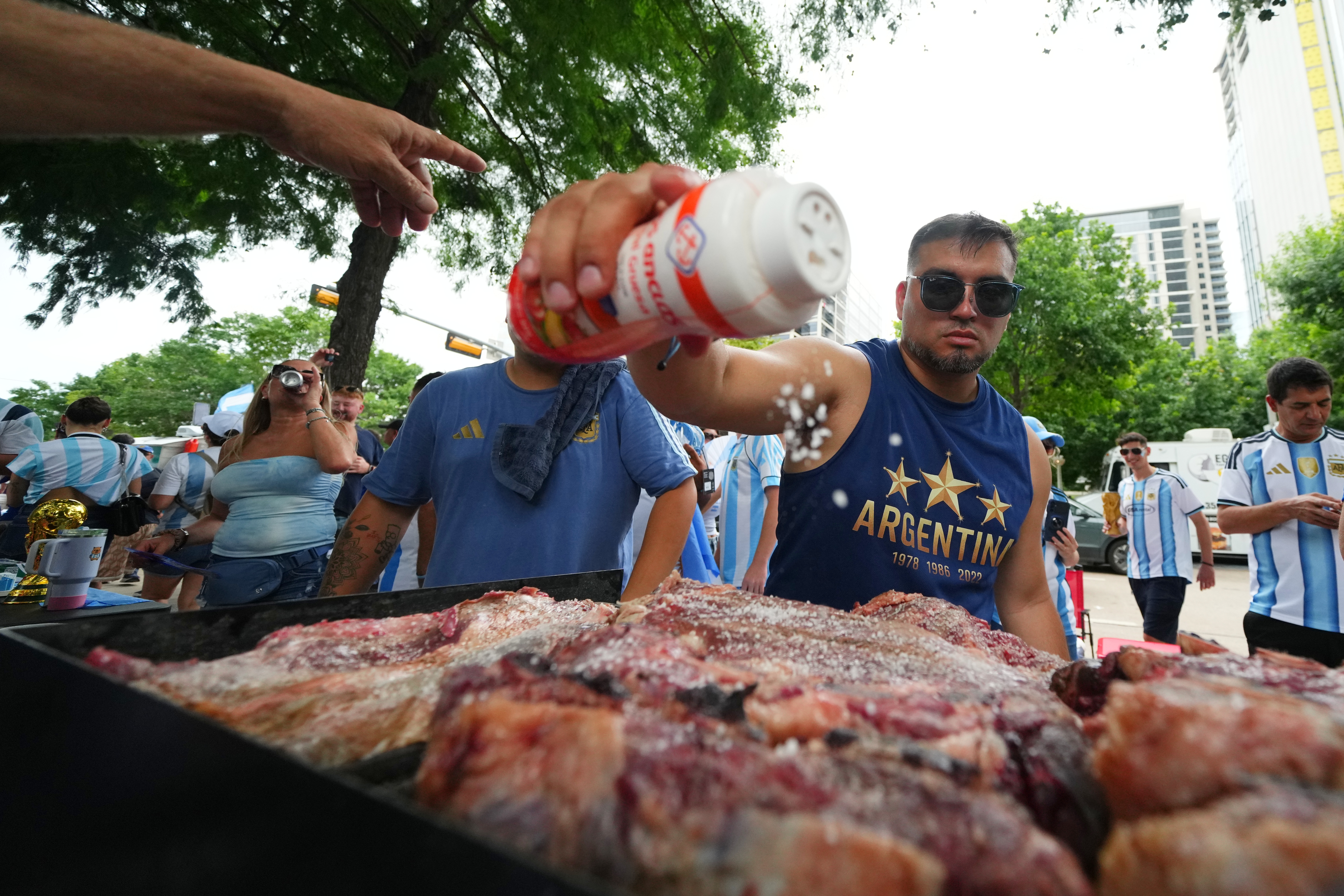 Lucas Martinez seasons meat with salt while grilling during a rally in Dallas, June 21, 2026.