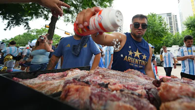 Lucas Martinez seasons meat with salt while grilling during a rally in Dallas, June 21, 2026.