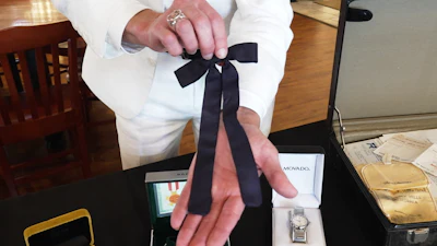 Auctioneer Jonathan Klunk shows a black bow tie worn by KFC founder Harland Sanders, Shelbyville, Ky., July 22, 2026.