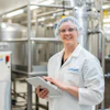 Lauren Zellner Standing In Front Of Equipment Smiling At Camera With Ipad