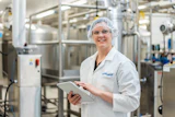 Lauren Zellner Standing In Front Of Equipment Smiling At Camera With Ipad