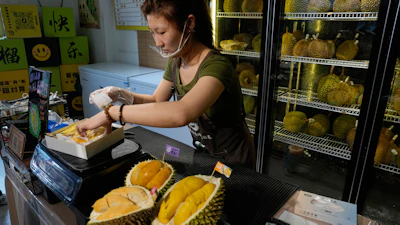 Worker Hou Yuxin packs durian fruit imported from Malaysia at a shop in Beijing, July 13, 2026.