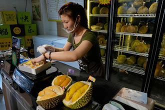 Worker Hou Yuxin packs durian fruit imported from Malaysia at a shop in Beijing, July 13, 2026.