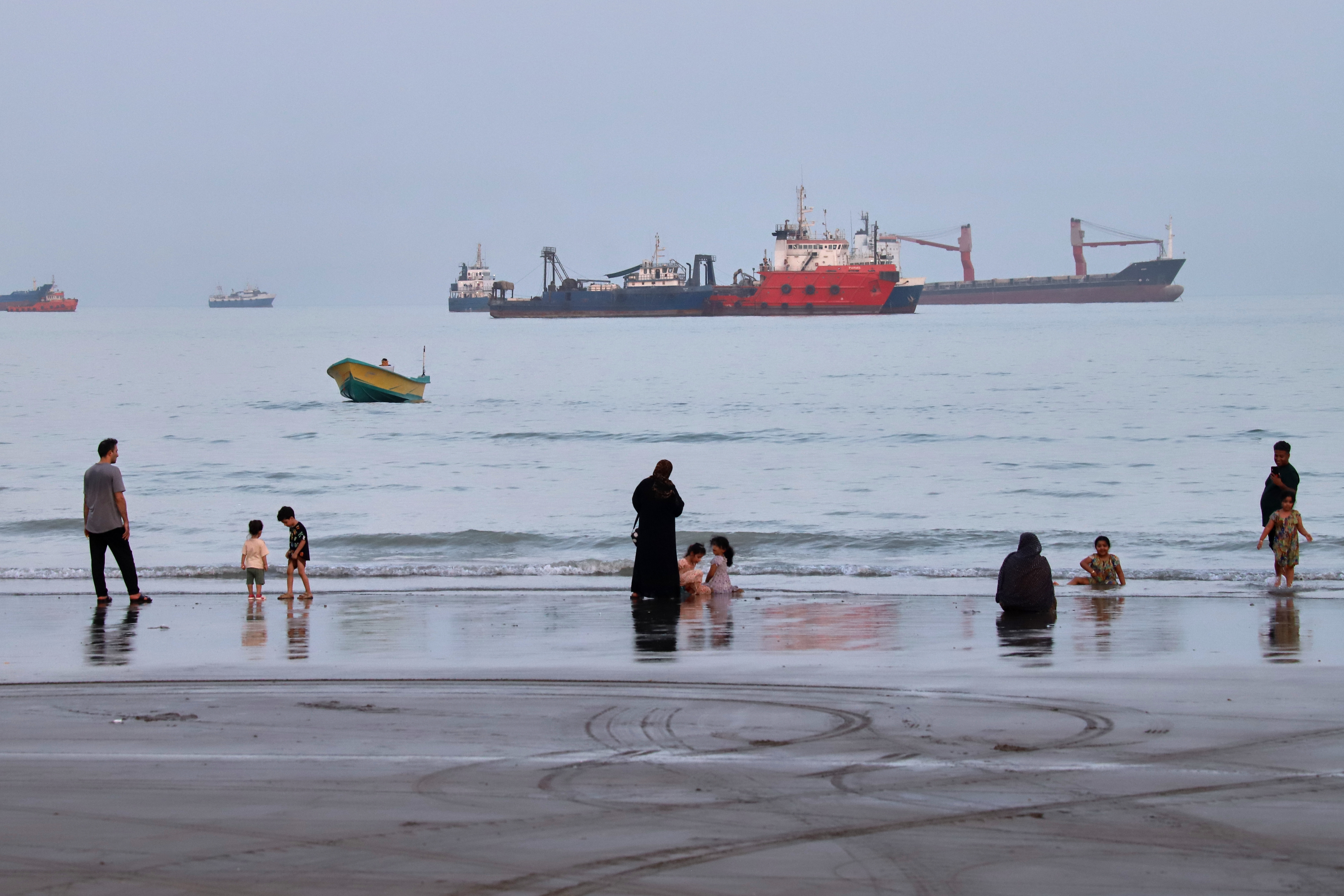 People spend time at a beach as commercial vessels are anchored in the Strait of Hormuz off Bandar Abbas, Iran, Aug. 5, 2026.