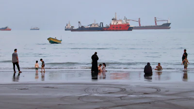 People spend time at a beach as commercial vessels are anchored in the Strait of Hormuz off Bandar Abbas, Iran, Aug. 5, 2026.