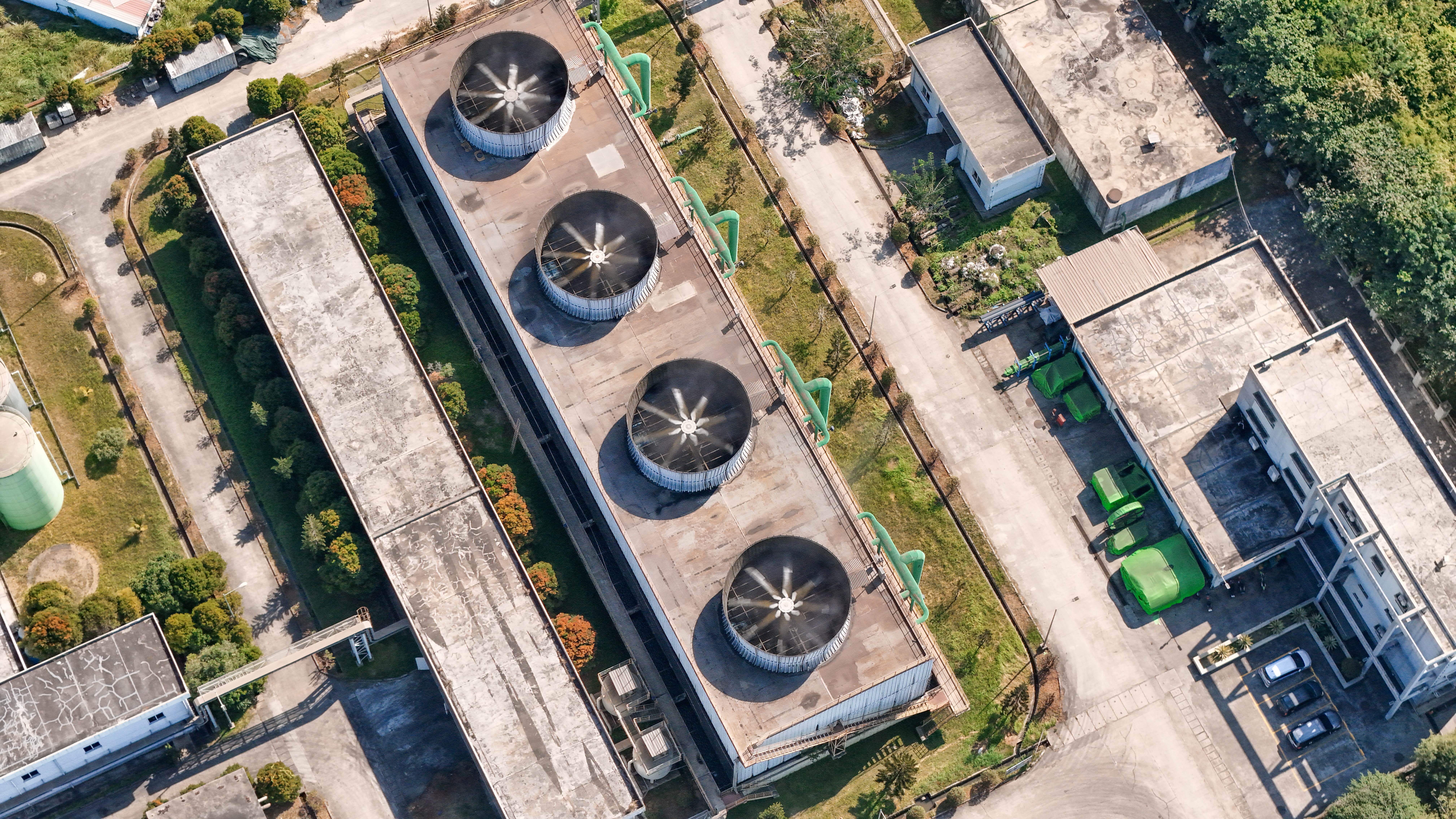 Aerial view of industrial facility with four circular cooling towers on rooftop surrounded by landscaped grounds and adjacent buildings