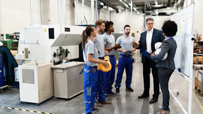 Manufacturing facility tour with workers and business professionals discussing near industrial machinery