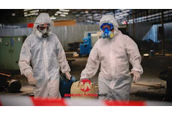 Two industrial workers in white protective suits and respirators at a manufacturing facility with Manufacturing Now logo