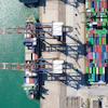 Aerial view of shipping port with cargo cranes, stacked containers, and docked vessel at waterfront terminal