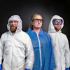 Three workers in protective suits and safety gear standing against dark background