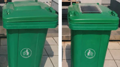 Two green recycling bins with white circular emblems on a paved outdoor surface