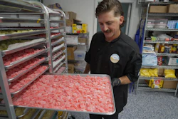 Worker holding tray of pink gummy candies in commercial kitchen with shelving and inventory