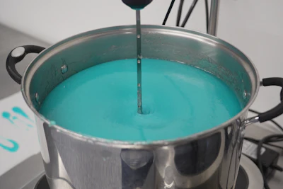 Stainless steel pot filled with turquoise liquid and a stirring utensil
