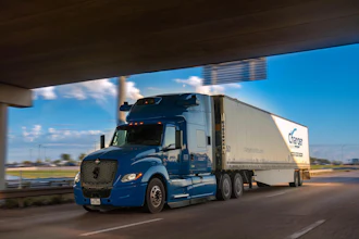 Blue Schneider semi-truck with white refrigerated trailer driving on highway under overpass