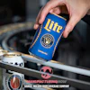 Hand holding blue Miller Lite beer can above industrial manufacturing equipment