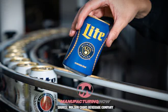 Hand holding blue Miller Lite beer can above industrial manufacturing equipment