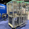 Hirata industrial manufacturing equipment with transparent enclosure and green frame on blue trade show floor