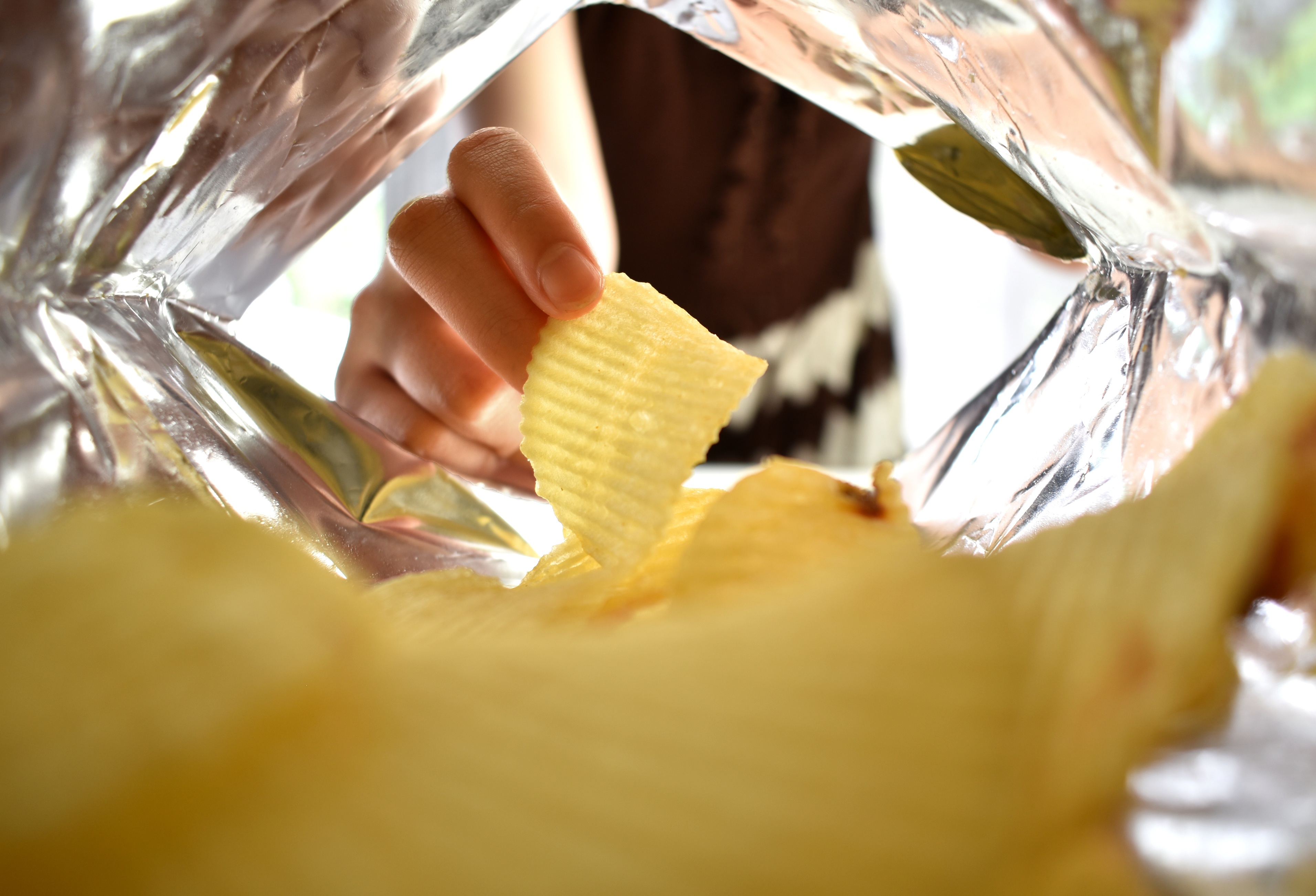 Hand holding a yellow ridged potato chip from inside a clear plastic bag