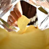 Hand holding a yellow ridged potato chip from inside a clear plastic bag