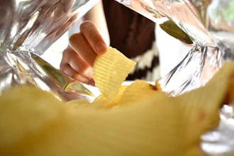 Hand holding a yellow ridged potato chip from inside a clear plastic bag