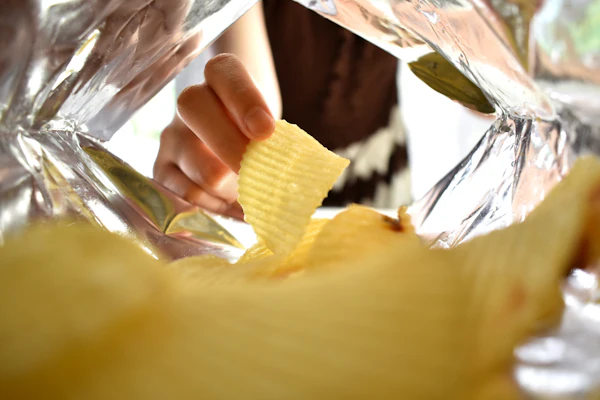 Hand holding a yellow ridged potato chip from inside a clear plastic bag