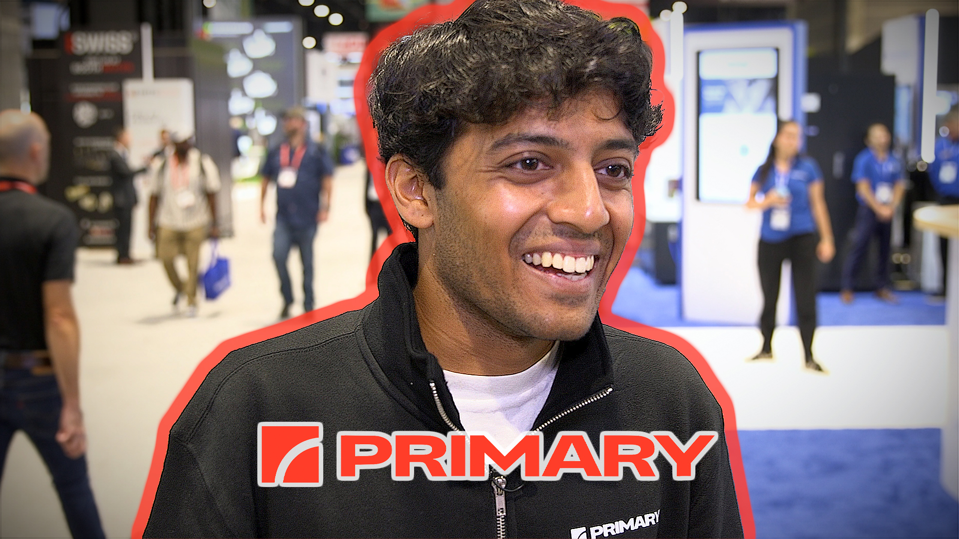 Smiling man wearing PRIMARY branded black jacket at indoor event or trade show