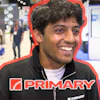 Smiling man wearing PRIMARY branded black jacket at indoor event or trade show