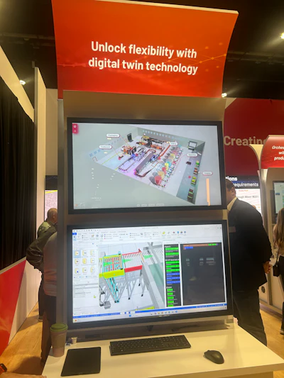 Trade show booth displaying digital twin technology with dual monitors showing 3D factory simulation and CAD software interface